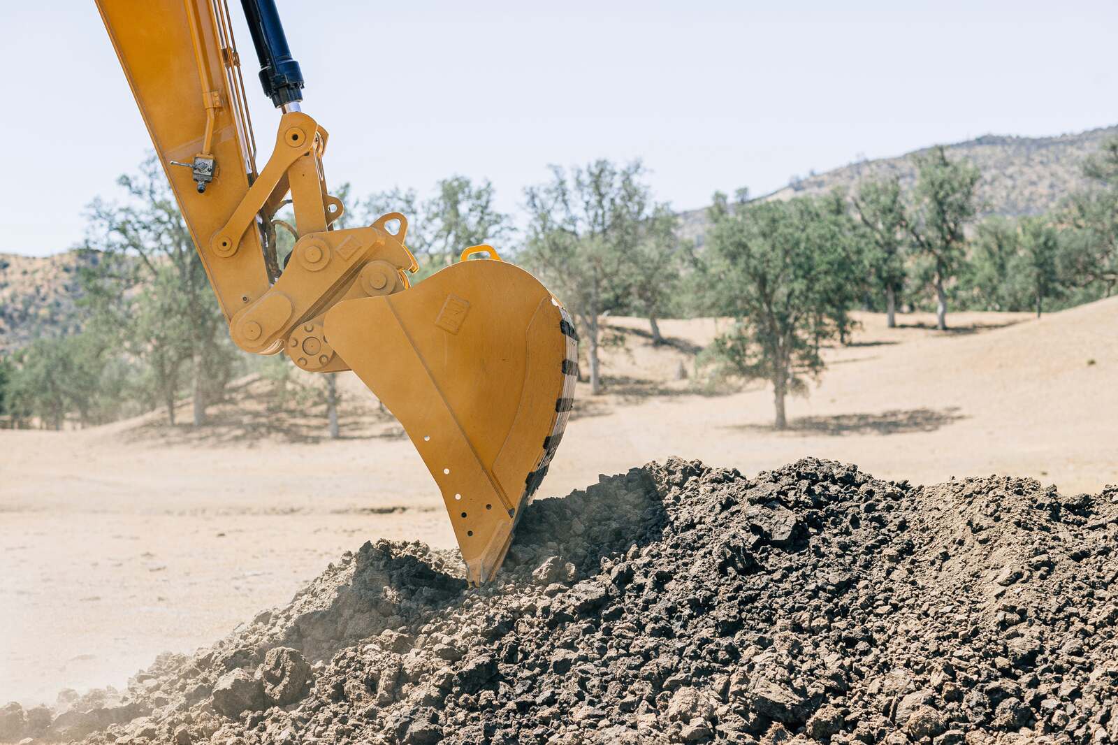 Excavator bucket digging soil at a construction site with trees in the background – heavy equipment attachment in action