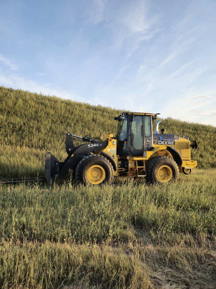 John Deere 524K-II wheel loader with pallet forks from Plains Equipment Rentals in Western Canada for sale, side view in field