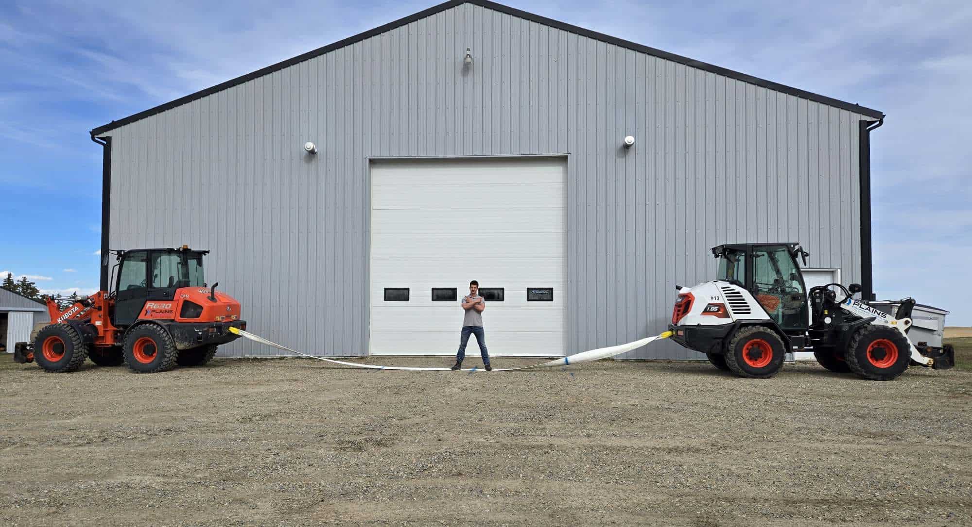 Two heavy equipment loaders demonstrating cable strength outside industrial warehouse building